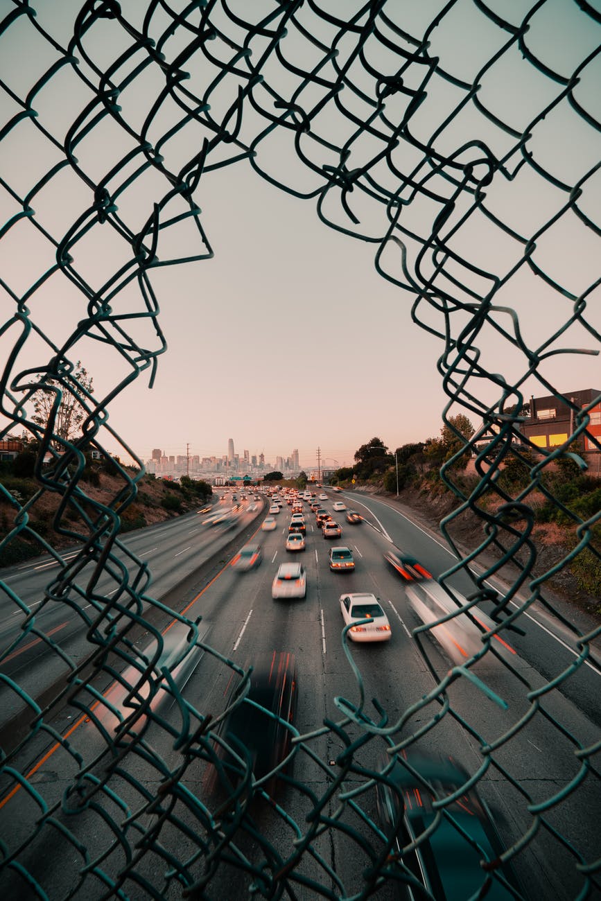 Open freeway with rush hour traffic and hole in chainlink fence  Kehn Hermano on Pexels.com